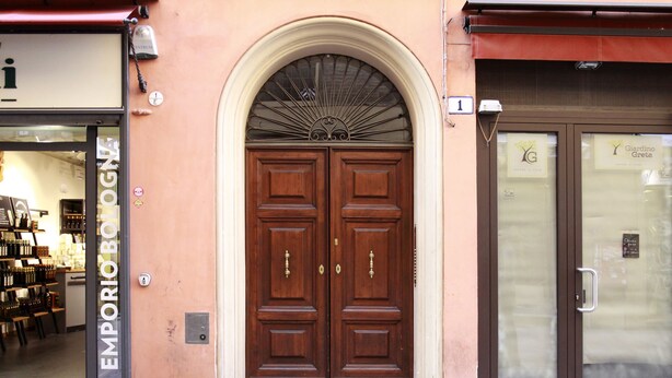 A double wooden door with a fanlight above it, set in a building with a beige facade. - Casa Isolani Piazza Maggiore (Bologna)