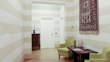A room with striped walls, a wooden floor, a green armchair, a table with magazines, and a hanging tapestry.