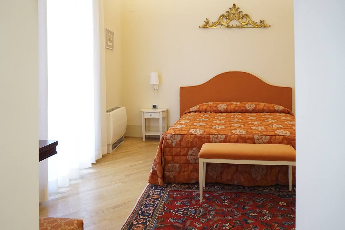 Un dormitorio con una cama, una mesita de noche, una lámpara y un banco.