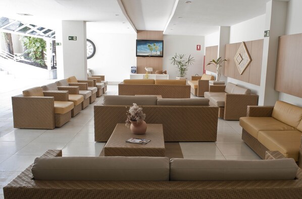 A spacious lobby with multiple seating areas, a large wall-mounted TV, and a staircase leading to an outdoor area.