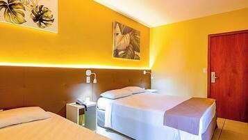 Quarto de hotel com duas camas, cabeceira de madeira, mesa de cabeceira e um quadro na parede.