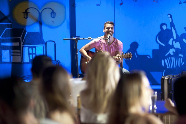 Una persona tocando la guitarra sobre un escenario, con un micrófono.