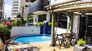 A rooftop pool with a waterfall, surrounded by lounge chairs and potted plants. - Ara Mar Praia Hotel (Fortaleza)