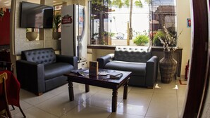 A living room with two sofas, a coffee table, a flat-screen TV, and a large window with a view of palm trees and parked cars. - Ara Mar Praia Hotel (Fortaleza)