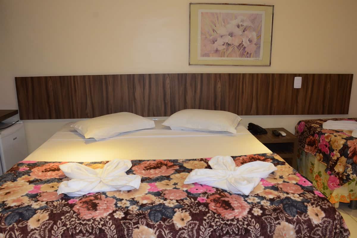 Ein Hotelzimmer mit Bett, Nachttisch, Telefon und einem gerahmten Blumenbild an der Wand.