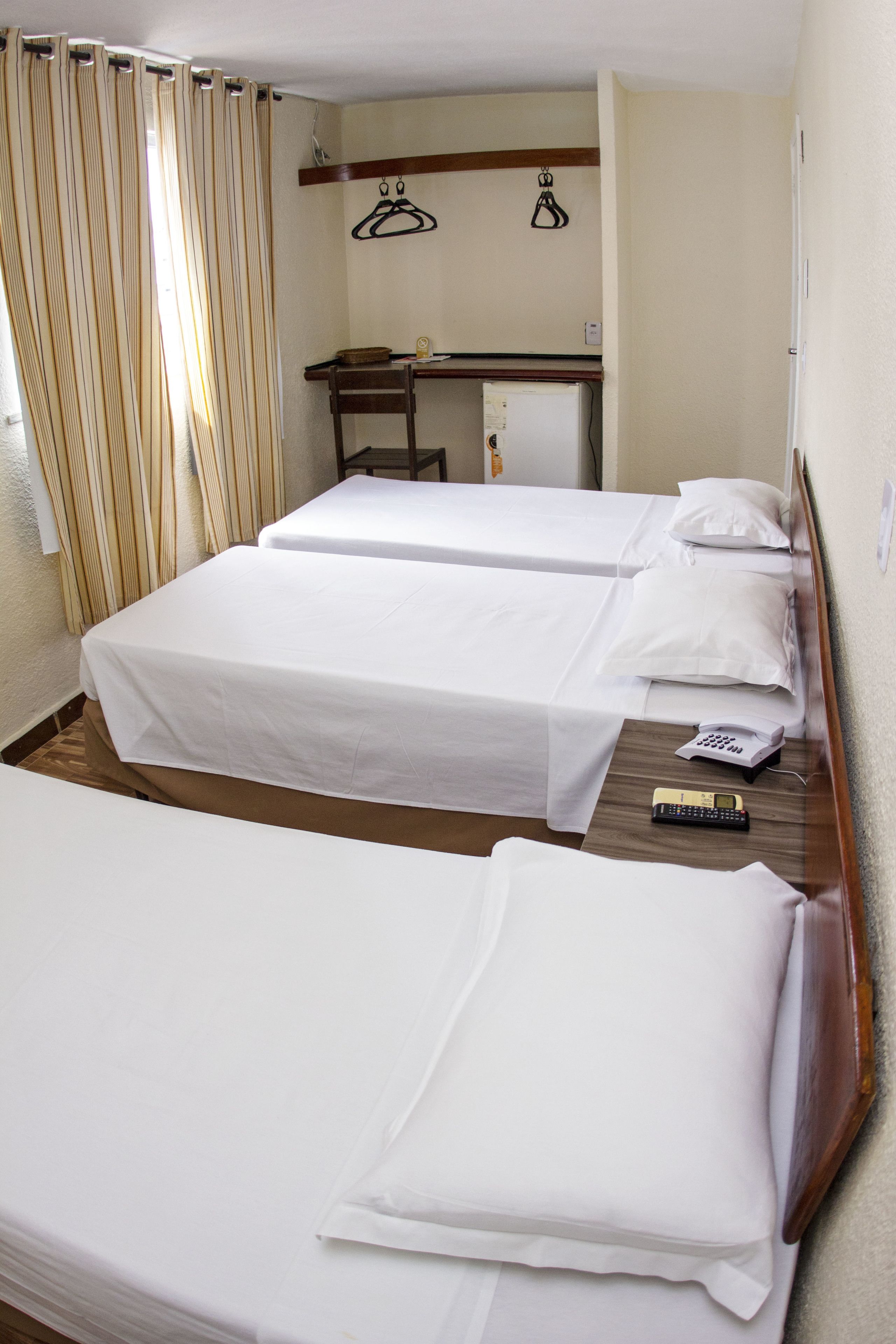 A hotel room with two single beds, a desk with a chair, a telephone, and a hanging coat rack.