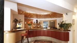 A modern reception area with a curved counter, a wooden ceiling, and a large decorative rug. - Hotel Hubertushof (Naz Sciaves)