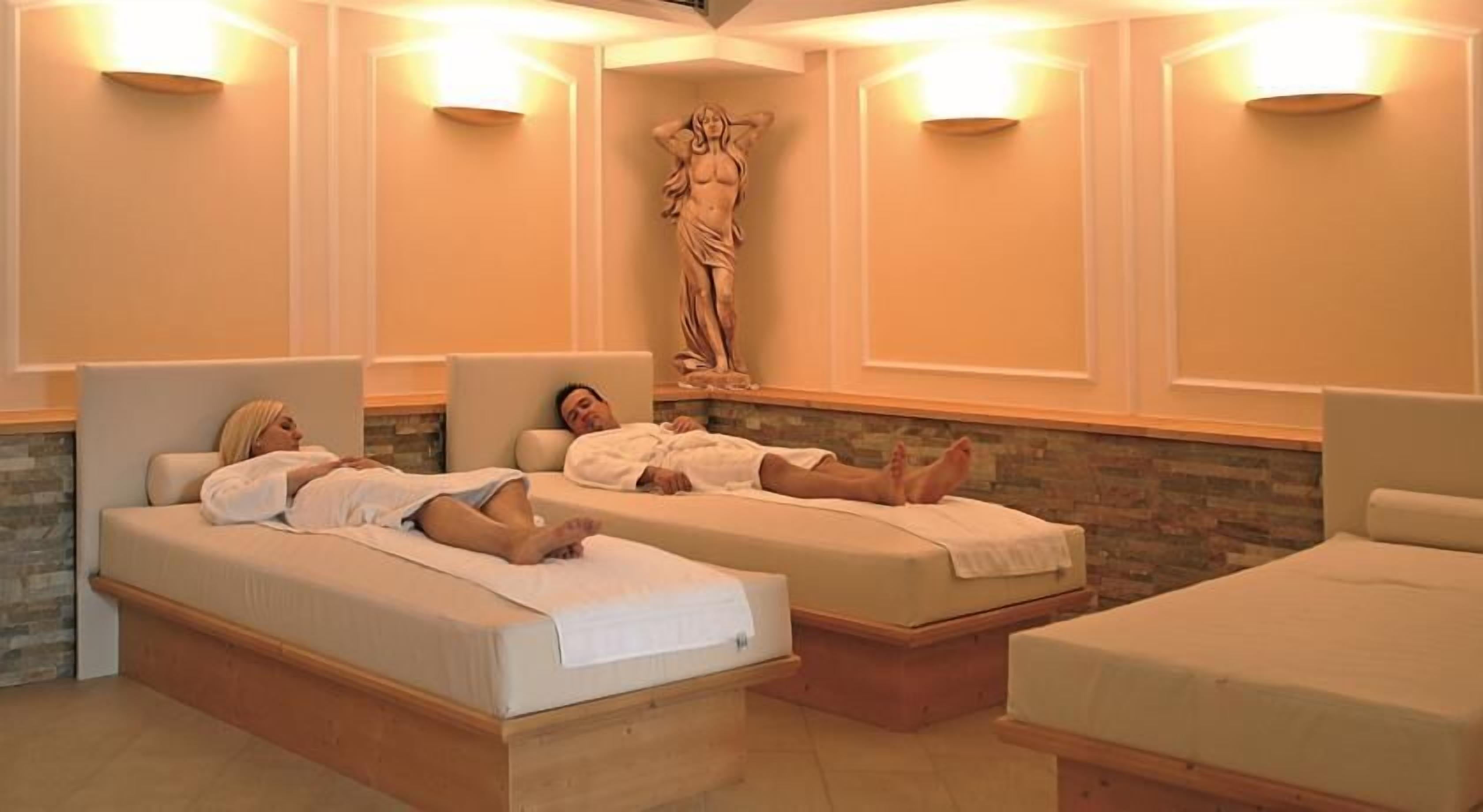 A spa room with two beds, a statue, and wall-mounted lights.