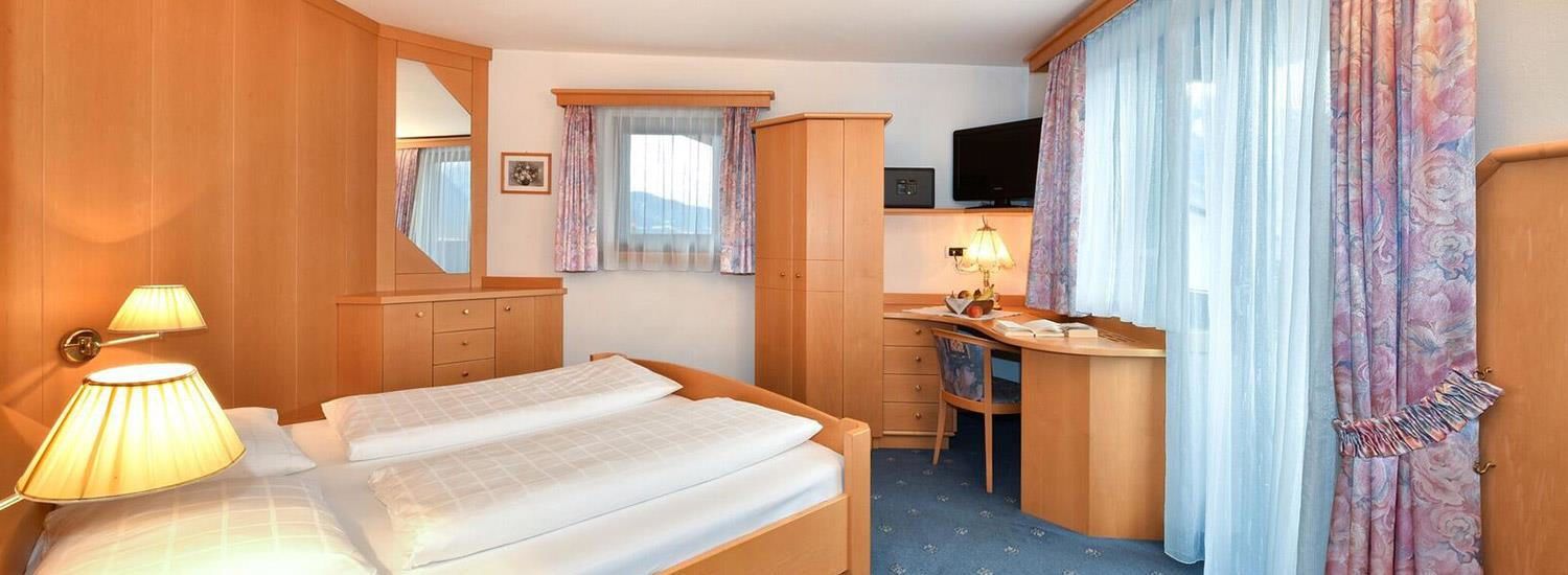 A hotel room with a bed, a desk, a television, and a window with curtains.