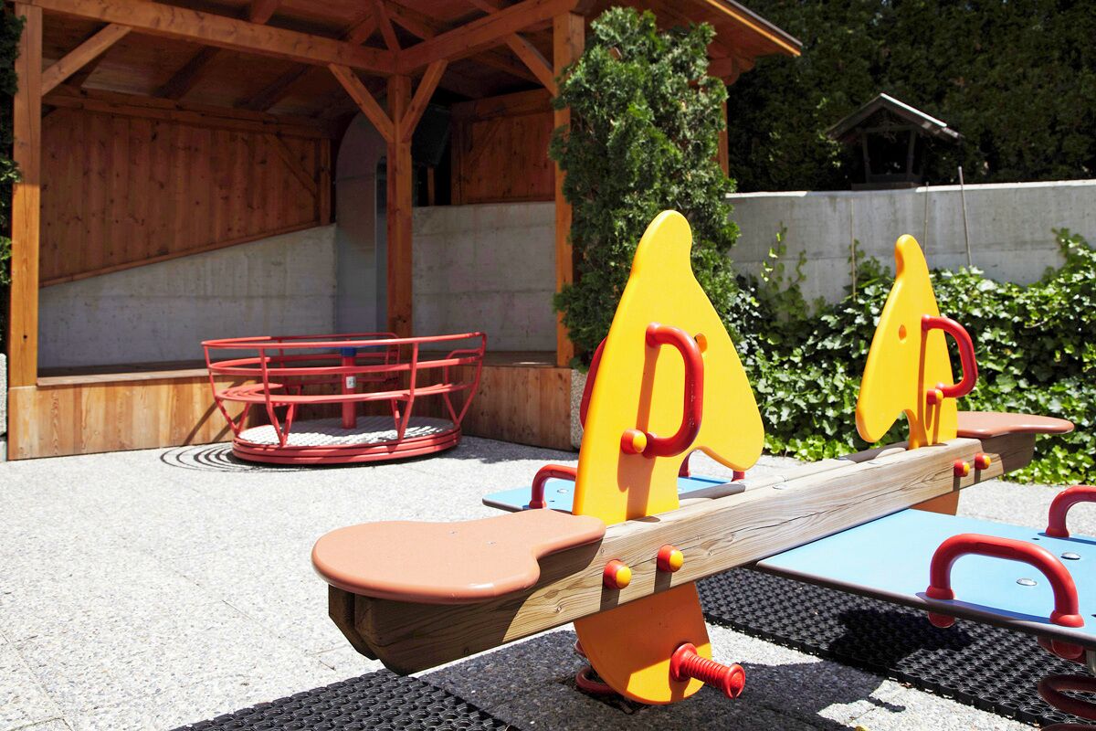 Un patio de juegos al aire libre con balancines y una estructura roja.