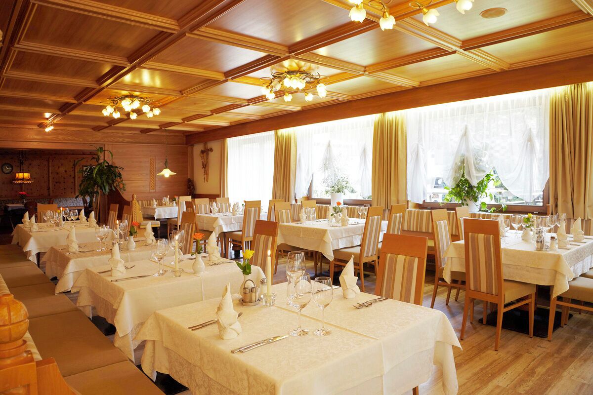 Una sala ristorante con diversi tavoli apparecchiati, caratterizzata da pannelli in legno e lampadari.