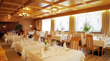Una sala ristorante con diversi tavoli apparecchiati, caratterizzata da pannelli in legno e lampadari.