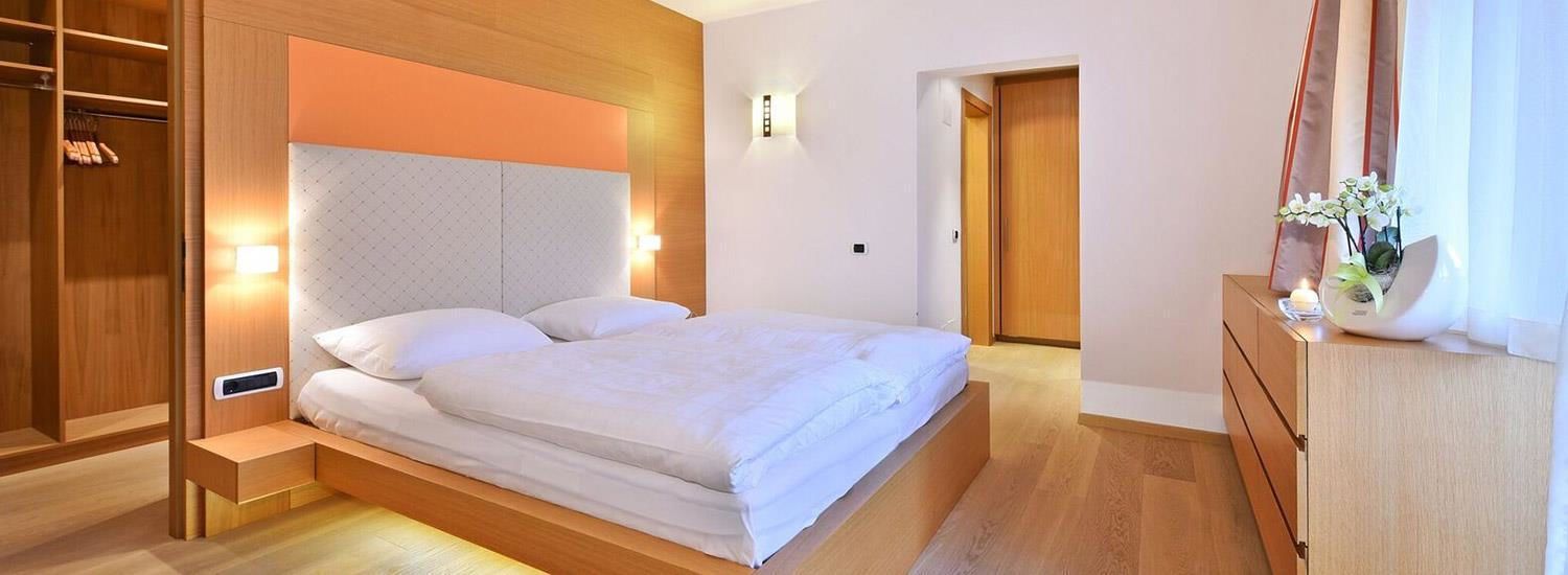 Un dormitorio moderno con cama, armario de madera y mesita de noche con planta.