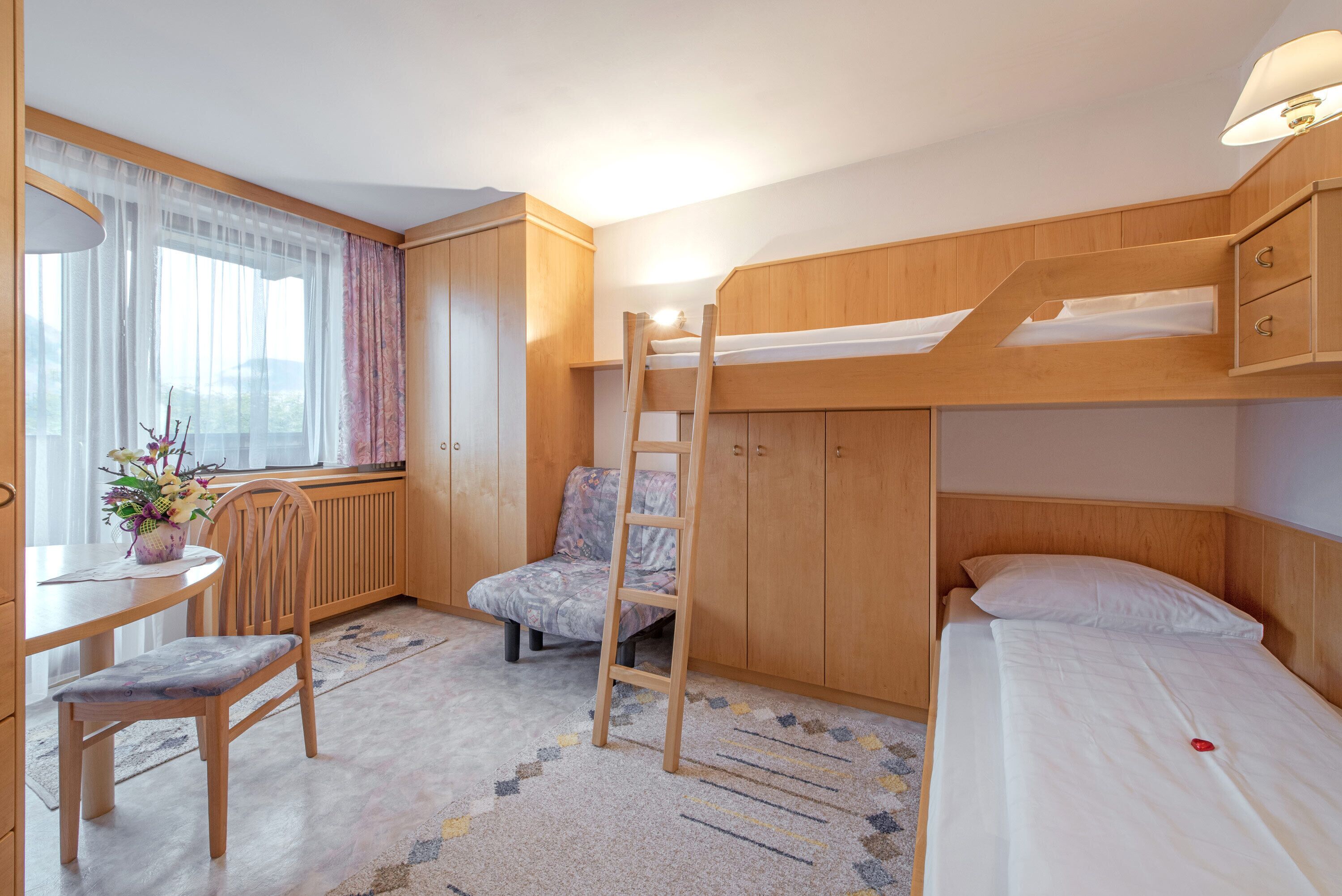 Une chambre avec un lit superposé, un bureau, une chaise et une fenêtre avec des rideaux.