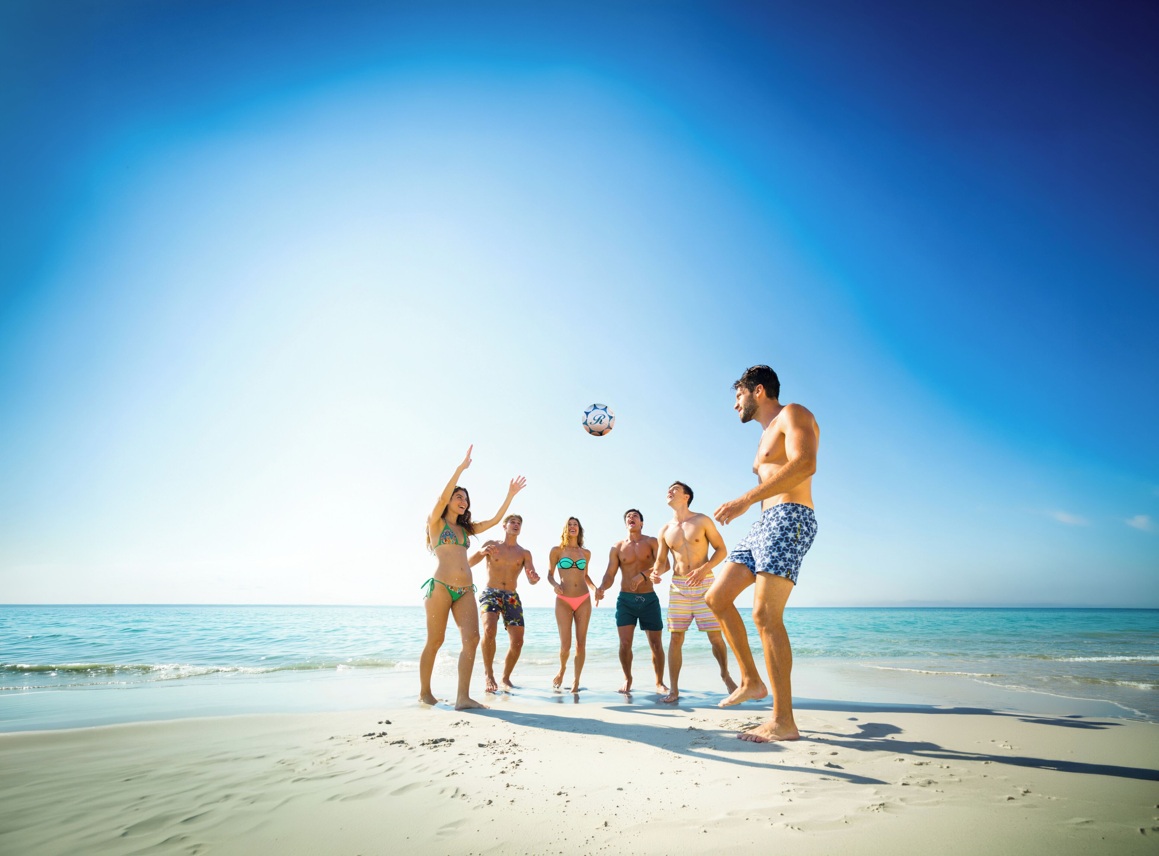 A group of people playing soccer on a beach.