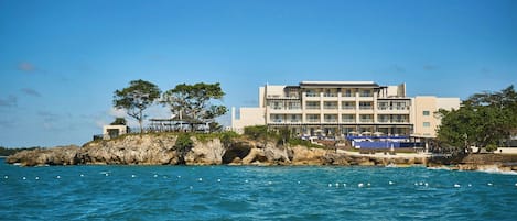A coastal hotel with multiple balconies, a rocky shoreline, and a view of the sea.