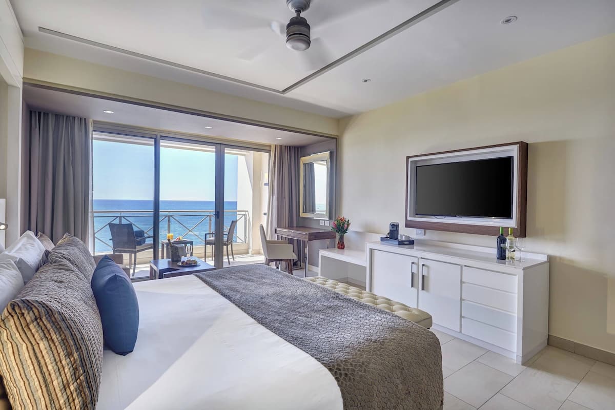 Une chambre d’hôtel avec un grand lit, un bureau, une télévision et un balcon donnant sur la mer.