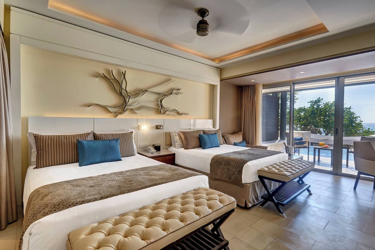Une chambre d’hôtel avec deux lits, une grande fenêtre et un balcon donnant sur la piscine.