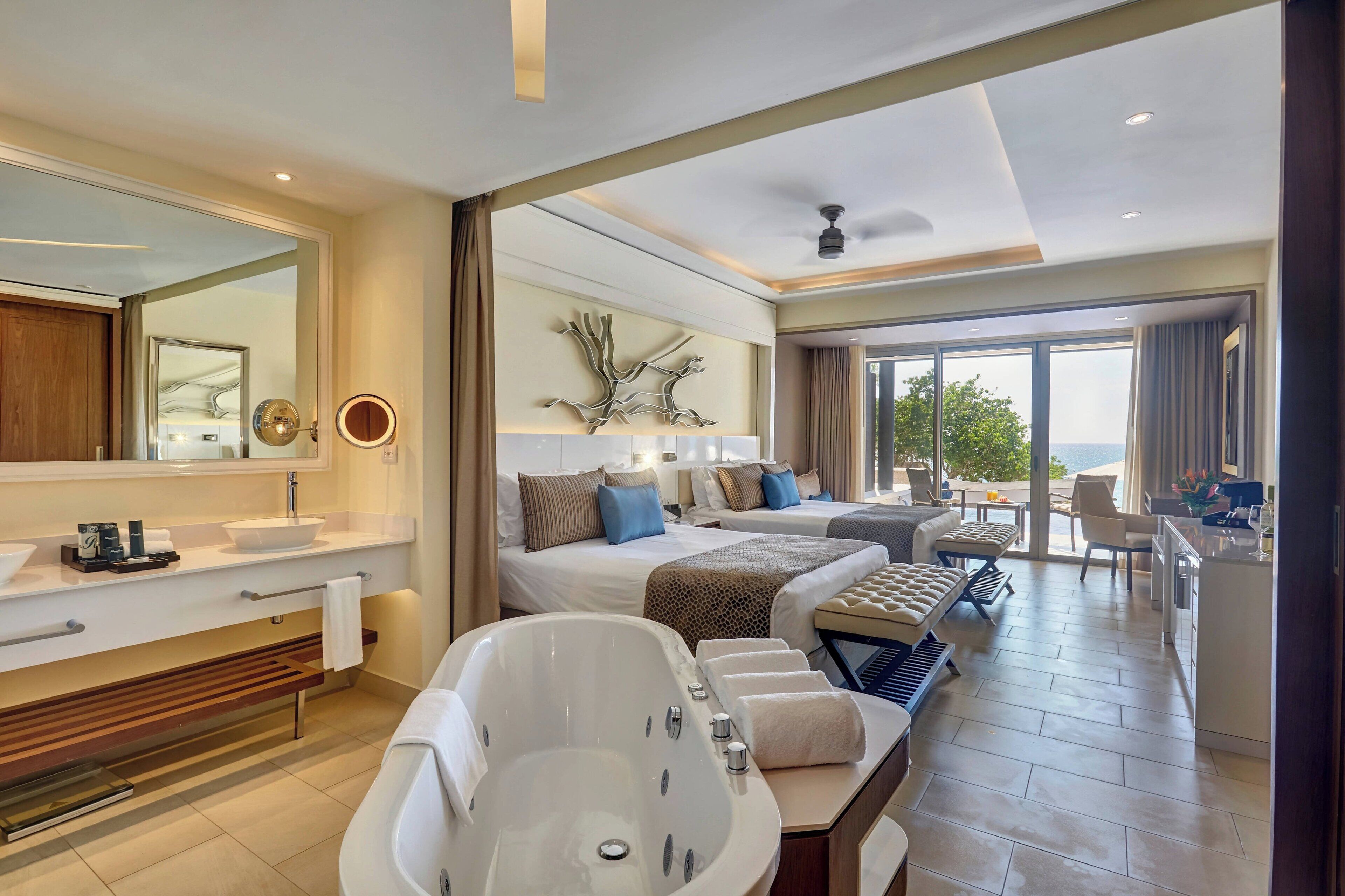 Habitación de hotel moderna con una bañera grande, zona de comedor separada y balcón con vistas.