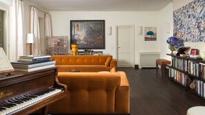 A living room with a piano, orange sofa, and a bookshelf. - Buonanotte Garibaldi (Rome)