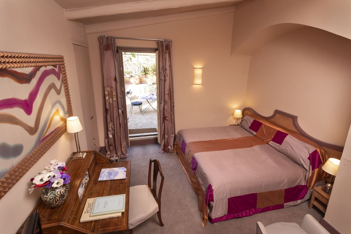 Habitación de hotel con cama, escritorio y silla, un florero y vistas al exterior.