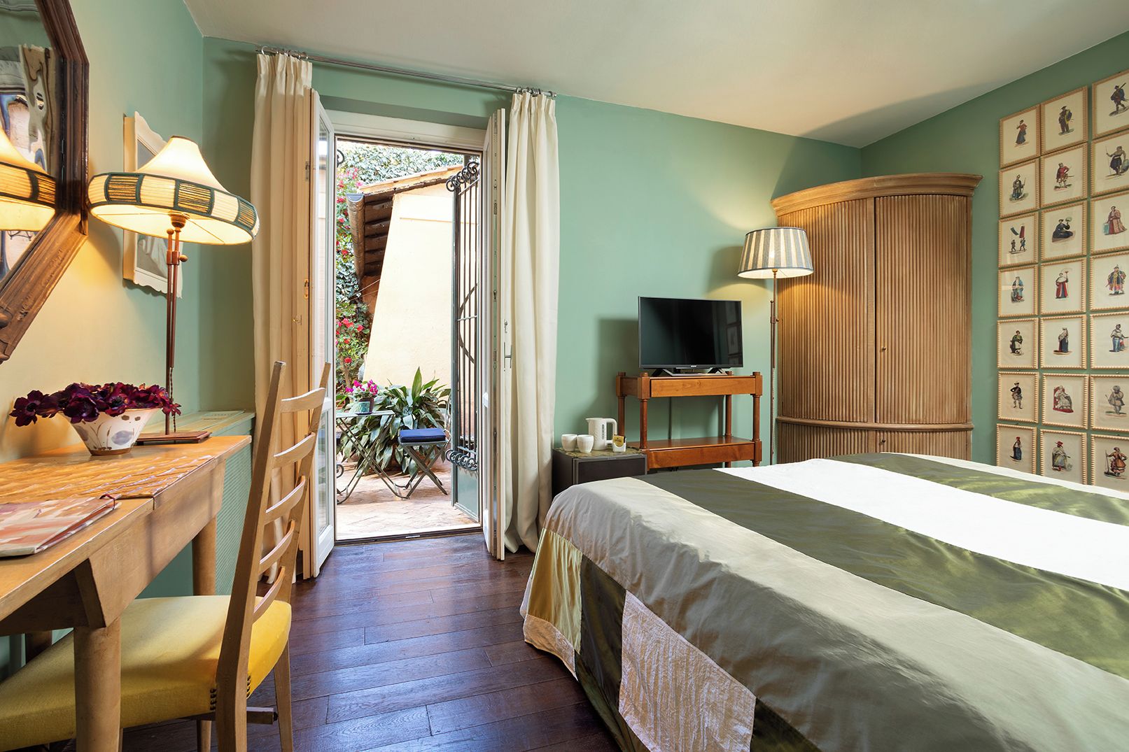 Ein Schlafzimmer mit Bett, Schreibtisch, Stuhl, Fernseher und einem Balkon mit Pflanzen.