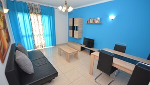 A modern living room with a sofa, coffee table, TV, and a dining area with chairs and a table. - Apartamentos Cravinho (Albufeira)