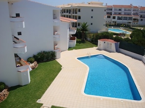 A swimming pool with a tiled deck, surrounded by a well-maintained lawn and a multi-story building with balconies. - Apartamentos Cravinho (Albufeira)