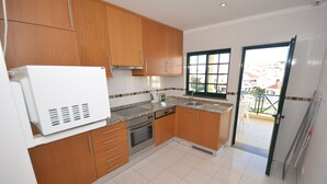 A kitchen with wooden cabinets, a stainless steel oven, and a window with a view of buildings. - Apartamentos Cravinho (Albufeira)