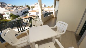 A balcony with a white table and four chairs, overlooking a residential area with white buildings. - Apartamentos Cravinho (Albufeira)
