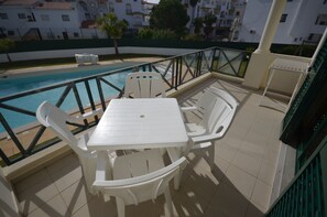 A terrace with a pool, white plastic furniture, and a view of buildings in the background. - Apartamentos Cravinho (Albufeira)