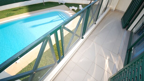 A balcony with a view of a swimming pool, a tiled floor, and a green railing. - Apartamentos Cravinho (Albufeira)