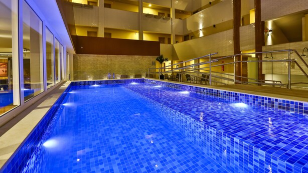 An indoor swimming pool with a blue tiled floor, surrounded by a high ceiling with multiple balconies. - Arcus Hotel Aracaju by Atlantica (Aracaju)