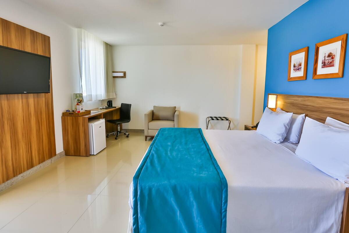 Een hotelkamer met een bed, een bureau, een stoel, een televisie en ingelijste foto's aan de muur.