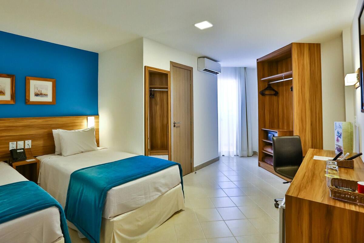 Een hotelkamer met twee bedden, een bureau, een kledingkast en een badkamer die door een open deur zichtbaar is.