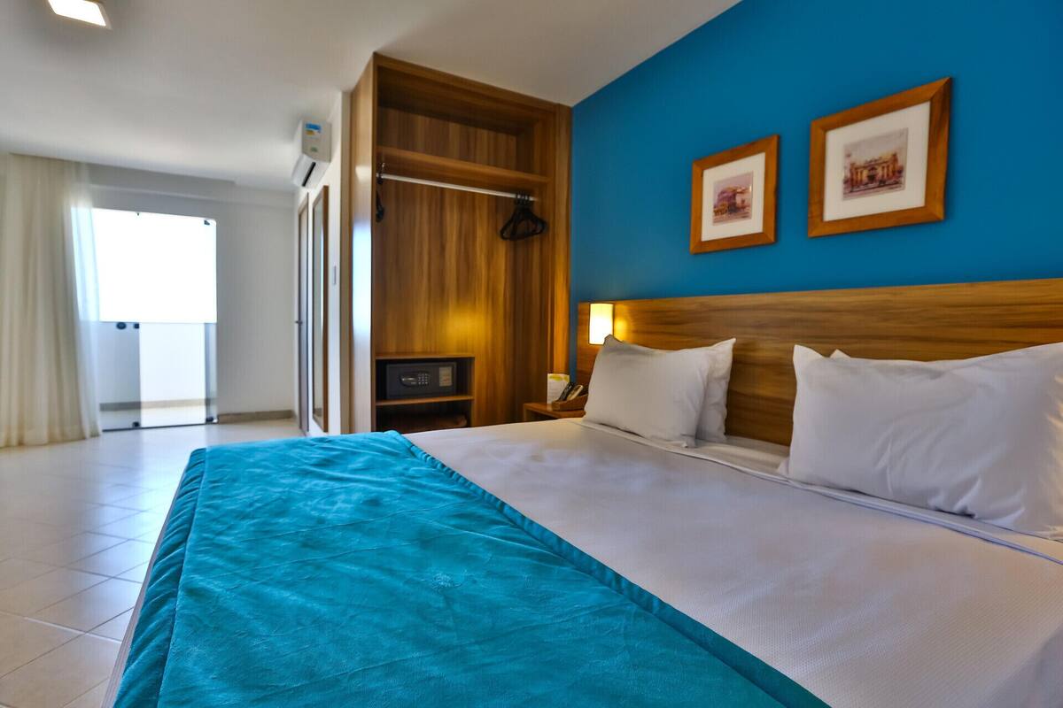 Een hotelkamer met een bed, een houten garderobe, een blauwe muur en twee ingelijste foto's.