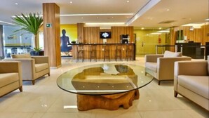 A modern lobby with a central glass coffee table, seating area with sofas, a reception desk, and a large plant. - Arcus Hotel Aracaju by Atlantica (Aracaju)