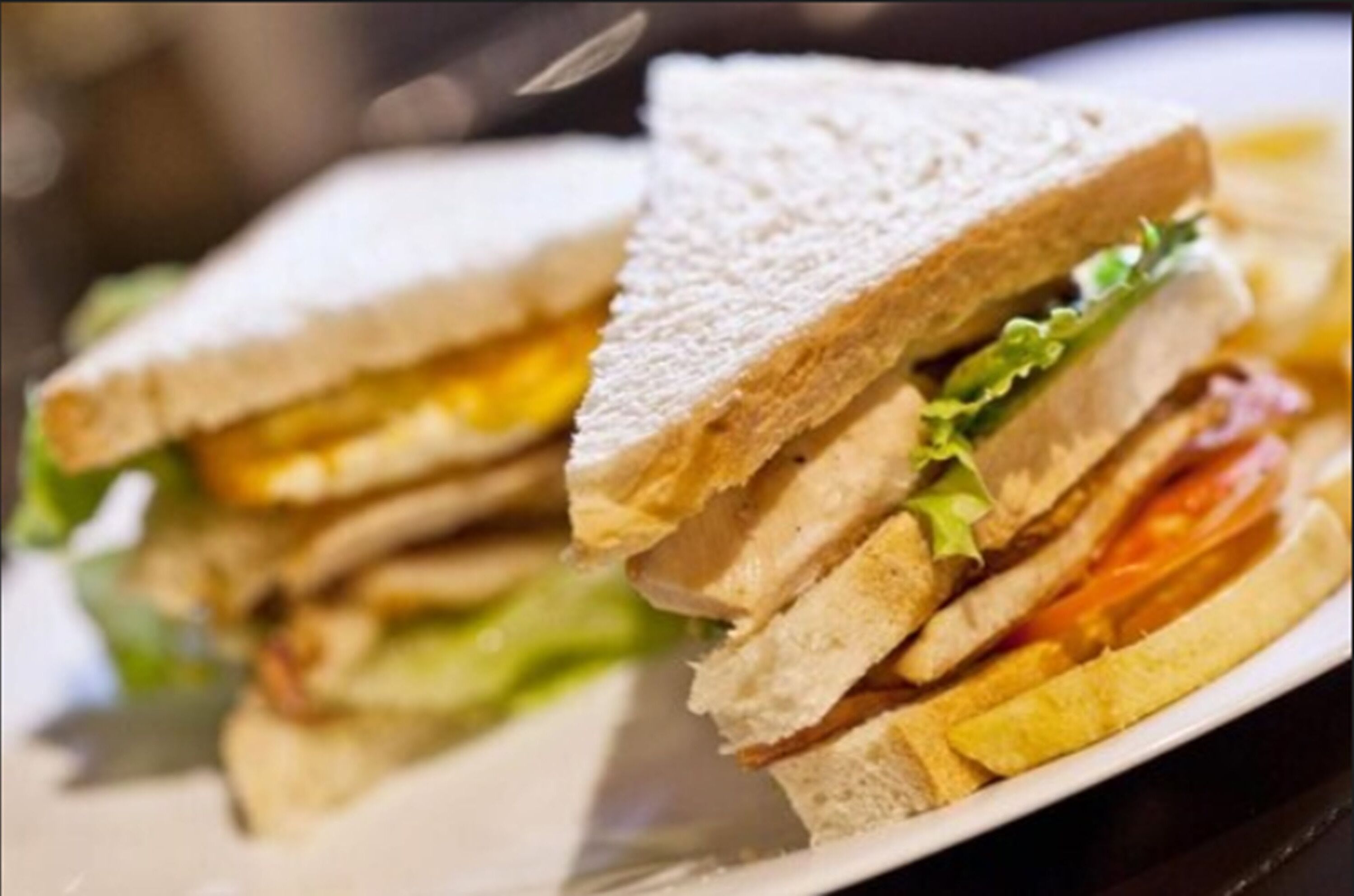 Un sándwich con lechuga, tomate y posiblemente queso, servido en un plato blanco.