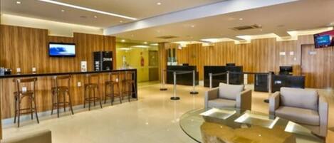 Een moderne lobby met een receptiebalie, een bar, zitplaatsen en een televisiescherm.