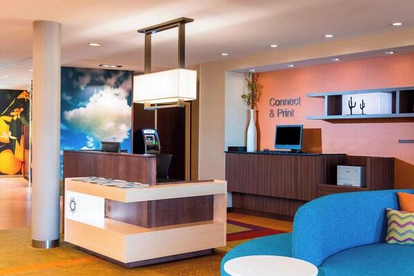 A reception desk with a digital kiosk, a blue sofa, and a wall with a 'Connect & Print' sign. - Fairfield by Marriott Inn & Suites Palm Desert Coachella Valley (Palm Desert)