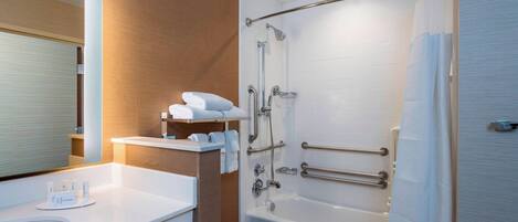 Un baño moderno con un lavamanos, espejo y bañera blancos. Hay toallas blancas y una cortina de ducha.