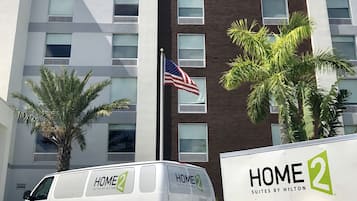 A hotel building with a sign reading "HOME 2 Suites by Hilton" and a white van parked in front.