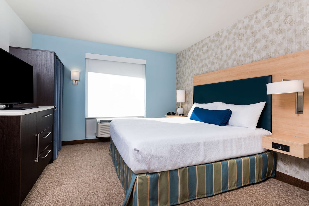 A hotel room with a bed, a desk, a TV, and a window.