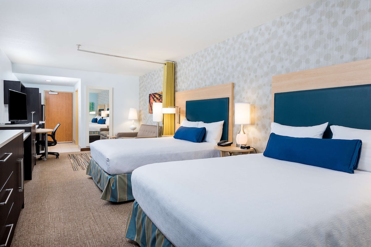 A hotel room with two beds, a desk, a TV, and a bathroom.