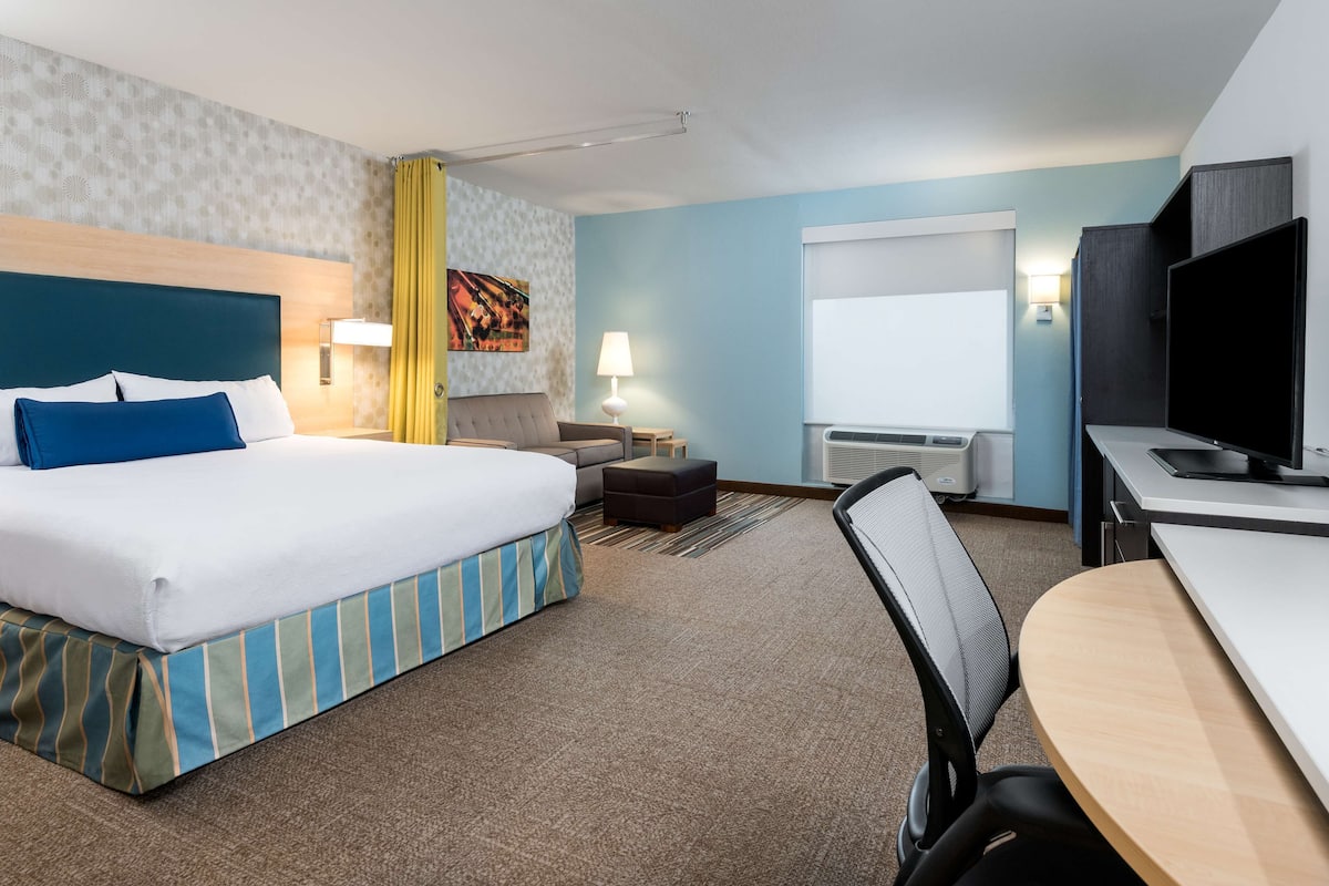 A hotel room with a large bed, a desk, a chair, a TV, and a window.