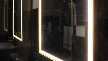 A modern bathroom with a large mirror, a gold faucet, and a potted plant.