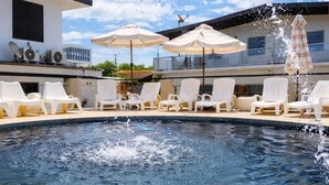 A swimming pool with lounge chairs and umbrellas, surrounded by a modern building. - Luichy's Seaside Hotel (Cabo Rojo)