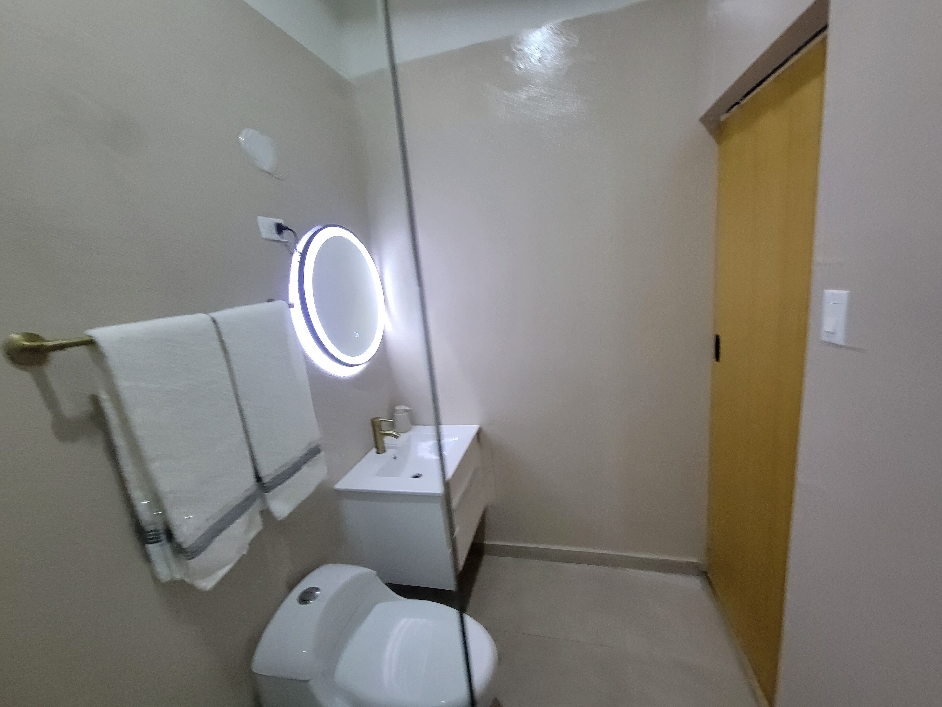 A small bathroom with a toilet, sink, and a mirror with lights.