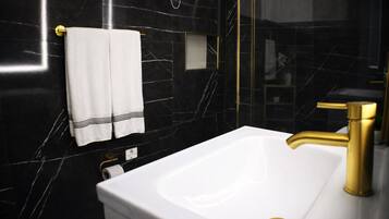 Un baño moderno con un lavamanos blanco, grifo dorado y paredes de mármol negro.
