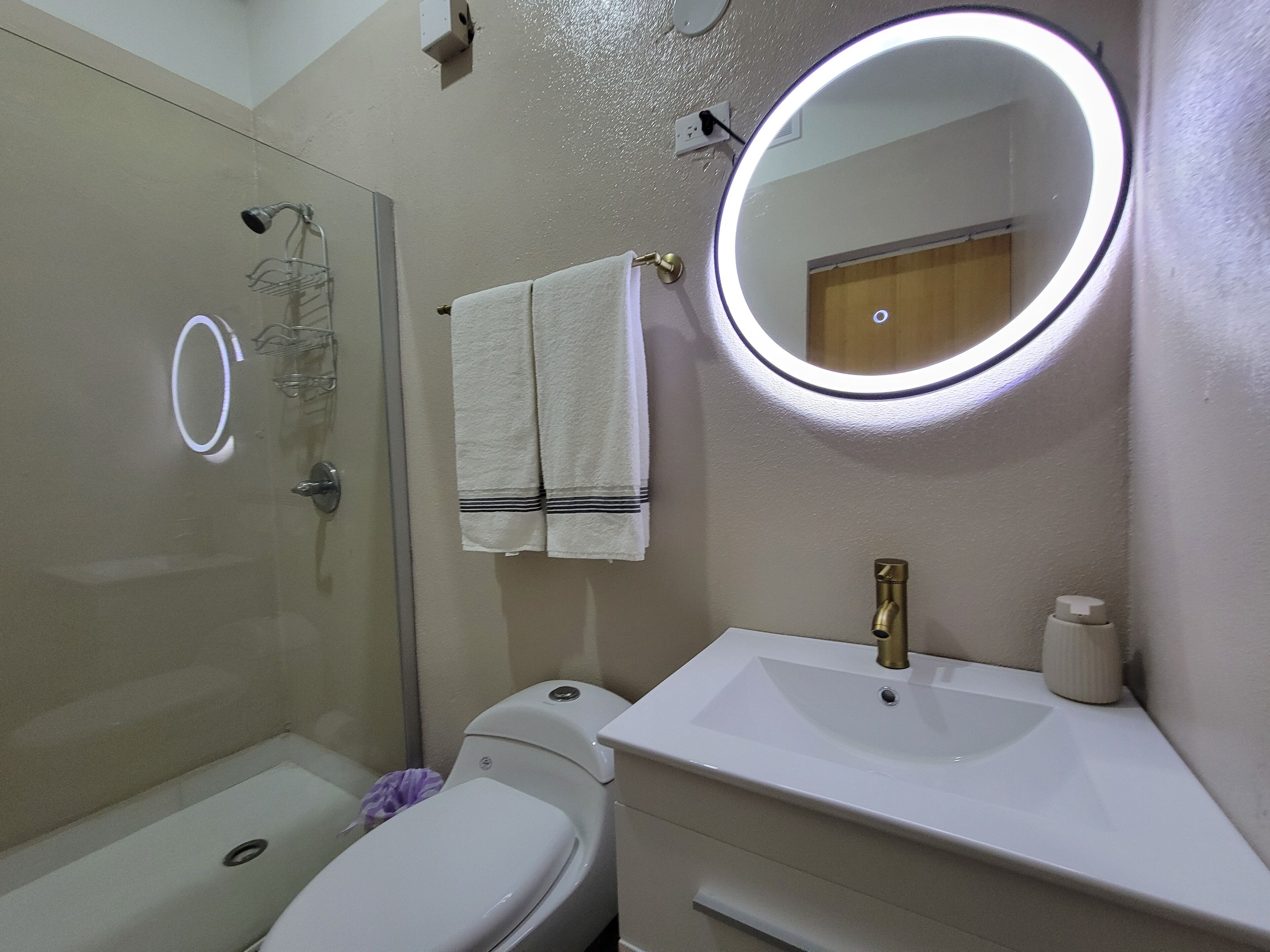 A bathroom with a glass shower enclosure, a toilet, a sink with a mirror, and a towel hanging on the wall.